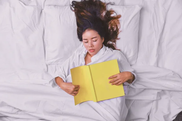 Молода жінка спить у ліжку. Верхній вид на молоду жінку, що добре спить у ліжку. Дівчина, яка читала книжку в ліжку і спала. Розслабся, розслабся, спиш, вчись, читай; книга, втіха, щасливий, глибокий сон. — стокове фото