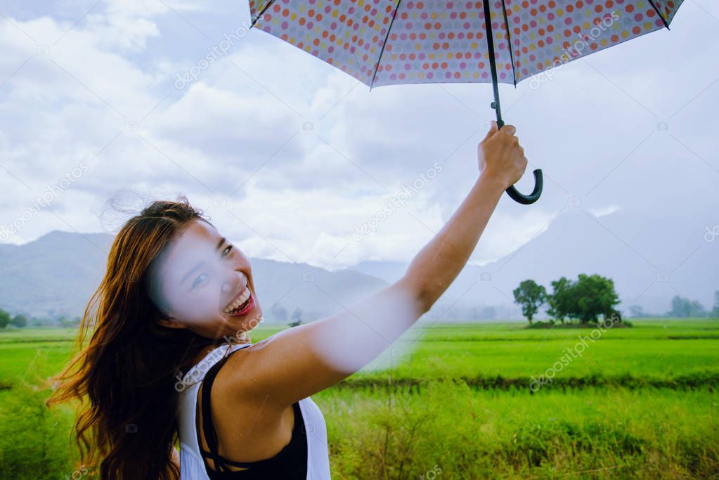 Asian women travel relax in the holiday. The women stood holds an umbrella in the rain happy and enjoying the rain that is falling. travelling in countrysde, Green rice fields, Travel Thailand.