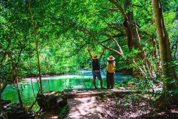 Travel couples with natural travel backpacks during the holidays. Couples traveling, relaxing in greens jungle and enjoying  the beautiful Emerald pond. Tourism hiking nature study.