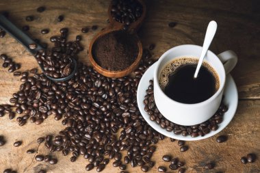 Eski bir mutfak masasının üstünde sade kahve. Arka plan konsepti, kahve fincanı ve kahve çekirdekleri ve ahşap masa. Kahve çekirdekleri masaya serildi..