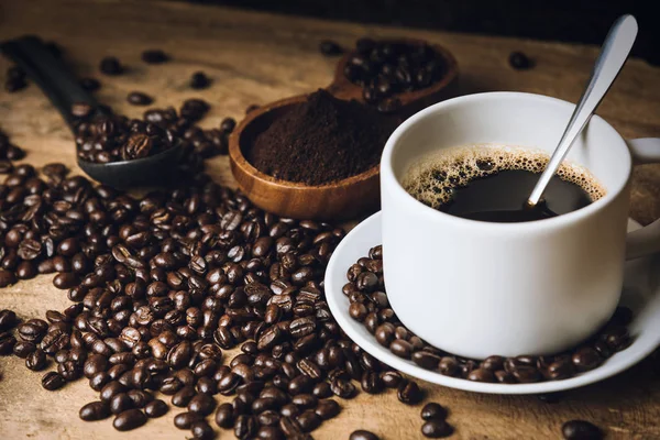 Vista superior Café preto quente em uma mesa de cozinha antiga. fundo conceito Xícara de café e grãos de café com pó moído sobre mesa de madeira. Grãos de café espalhados na mesa . — Fotografia de Stock