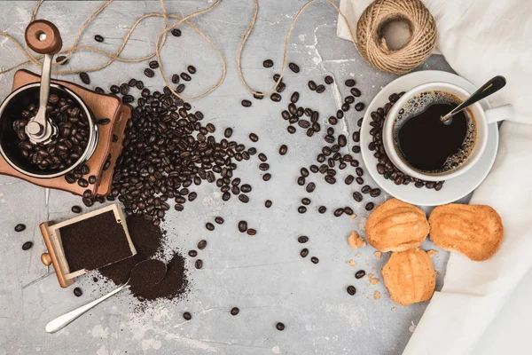 Kaffekopp, med kaffekvarn och kaffebönor med malet pulver på bordet. Ovanifrån Varmt kaffe och bakverk på ett gammalt köksbord. bakgrund koncept Kaffekopp och kaffekvarn med andra tillbehör. — Stockfoto