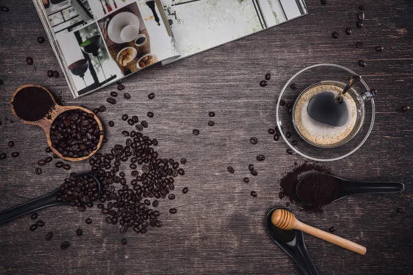 Bruna kaffebönor och en kopp varmt kaffe på ett träbord med honung. Trä bakgrund och espresso och bönor. Toppvy med kopieringsutrymme för din text. Böcker om kaffe. — Stockfoto