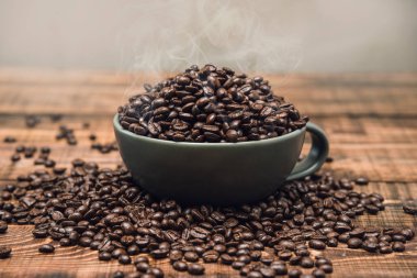 Koyu kahve taneleriyle dolu bir fincan kahverengi ahşap bir masanın üzerinde duruyor, arka plan resmi. Yeşil fincanda kahve çekirdeği..