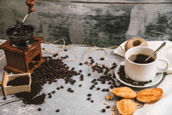 Kaffekopp, med kaffekvarn och kaffebönor med malet pulver på bordet. Ovanifrån Varmt kaffe och bakverk på ett gammalt köksbord. bakgrund koncept Kaffekopp och kaffekvarn med andra tillbehör. — Stockfoto