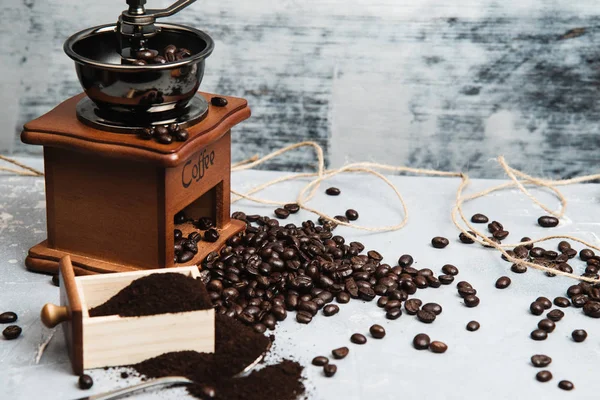 Kaffekopp, med kaffekvarn och kaffebönor med malet pulver på bordet. Sidovy Varmt kaffe på ett gammalt köksbord. bakgrund koncept Kaffekopp och kaffekvarn med andra tillbehör. — Stockfoto