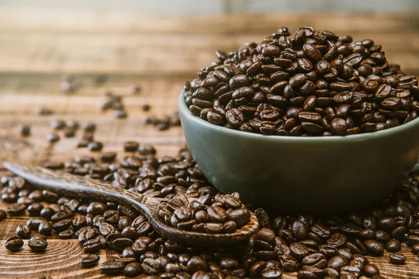 Cup full av svarta kaffekorn ligger på ett brunt träbord, bakgrundsbild. Kaffebönor i en grön kopp. — Stockfoto