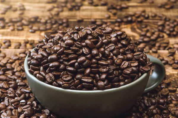 Copa llena de granos de café negro se encuentran en una mesa de madera marrón, imagen de fondo. Granos de café en una taza verde . — Foto de Stock