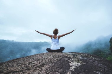 Genç kadın dağlarda yoga yapıyor. Asyalı kadın doğayı gezer. Seyahat rahatlama egzersizleri yoga dağ zirvesinde doğal sise dokunmak.