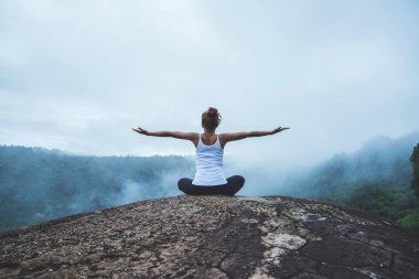 Genç kadın dağlarda yoga yapıyor. Asyalı kadın doğayı gezer. Seyahat rahatlama egzersizleri yoga dağ zirvesinde doğal sise dokunmak.