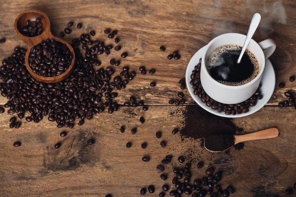 Vista superior Café preto quente em uma mesa de cozinha antiga. fundo conceito Xícara de café e grãos de café com pó moído sobre mesa de madeira. Grãos de café espalhados na mesa . — Fotografia de Stock