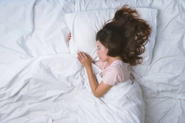 Genç kız dinleniyor. İyi geceler uyku konsepti. Sabahları beyaz bir odada pijama giyen bir kız yatakta uyuyor. sıcak ton.