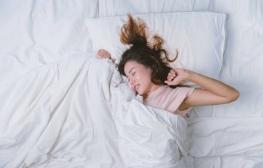 Genç kız dinleniyor. İyi geceler uyku konsepti. Sabahları beyaz bir odada pijama giyen bir kız yatakta uyuyor. sıcak ton.