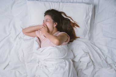 Genç kız dinleniyor. İyi geceler uyku konsepti. Sabahları beyaz bir odada pijama giyen bir kız yatakta uyuyor. sıcak ton.