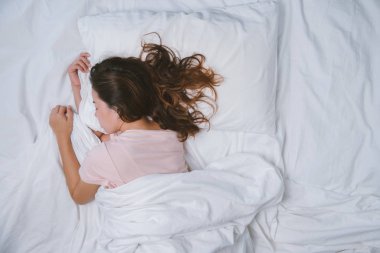 Genç kız dinleniyor. İyi geceler uyku konsepti. Sabahları beyaz bir odada pijama giyen bir kız yatakta uyuyor. sıcak ton.