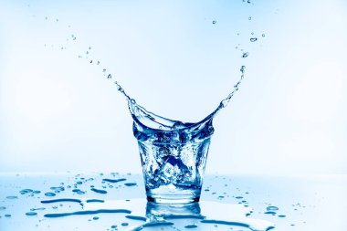 Bardağa düşen buz, mavi arka planda izole edilmiş camdan dökülen suyla.