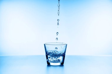 Mavi arka planda izole edilmiş camdan su sıçrıyor.