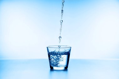 Mavi arka planda izole edilmiş camdan su sıçrıyor.