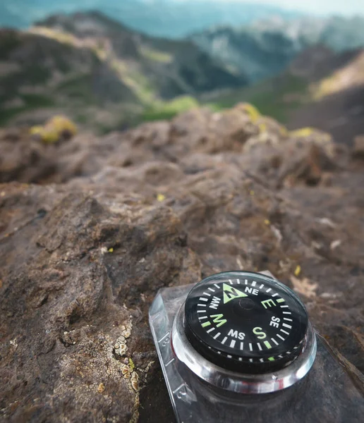 A close up of a compass on a rocky surface pointing north with mountains and valleys in the background in Switzerland