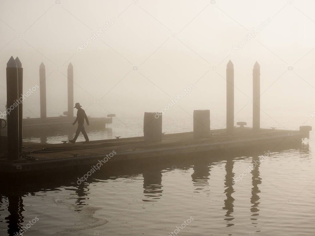 A silhouetted man working on the docks on a foggy morning with reflections in the water.