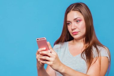 Kahverengi saçlı, mavi gözlü seyir için pembe telefon şaşkınlık yüz buruşturma ve hafif slmile ile genç beyaz kadınla. Mavi arka plan, stüdyo, izole, model, kopya alanı