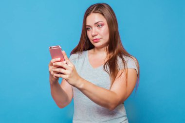 Kahverengi saçlı, mavi gözlü olan beyaz kadın şaşkınlık yüz buruşturma ve hafif slmile ile pembe telefona benziyor. Mavi arka plan, studio, model, izole. Uzay kopyalayın. Yüzünde güçlü duygular.