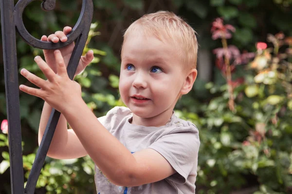 かなり Caucasuan 男の子は青い目とブロンドの髪 緑の葉と花の背景で かわいい顔に Funne — ストック写真