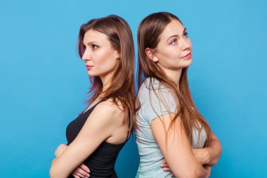 İki beyaz çekici genç kadın arka arkaya, geçti elleriyle ayağa. İkisi de esmer, kahverengi gözlü, ikinci mavi gözlü. İzole, kadar üzerinde parlak mavi arka plan, stüdyo yakın. 