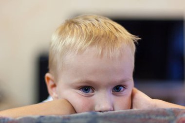 Işık altın saçlı ve mavi gözlü, melankoli izlenim, şirin küçük beyaz çocuk kafasını yaslanır portresi. Yakın yukarı, kapalı, oda. Gözde güçlü duygular.