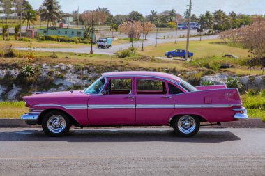 Havana / Cuba: Classic model pink Cadillac Fury from side proection, stats in front of a village landscape. clipart