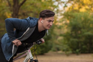 Çekici genç beyaz adam parkta bisiklet koyu saçlı. Beyaz kulaklık / kulaklık, favori müzik. Açık havada, altın yaprakları. Erken sonbahar / arka plan Güz. Sağlıklı yaşam konsepti, spor, fitness, çeşitlilik insanlar. Kopya alanı