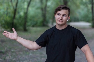 Çekici genç beyaz adam cep telefonu ve bisiklet yeşil parkta tutar. Beyaz kulaklık, küpe, yüzük, karanlık rahat kıyafet, siyah saçlı. Terk edilmiş park arka plan. Açık havada, yakın çekim, alanı Kopyala. Olumlu duygular ifade ilginç,.