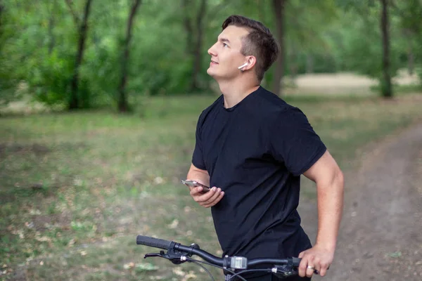Viehättävä Nuori Valkoihoinen Mies Pitää Matkapuhelinta Polkupyörää Vihreässä Puistossa Valkoiset — kuvapankkivalokuva