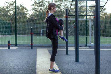 Park spor zemin üzerinde beyaz kadın ısıtır. Kız kapağı siyah spor giyim, spor poz (bacak). Çok atletik şekli. Uzay kopyalayın. Eğitim için hazırlanıyor.