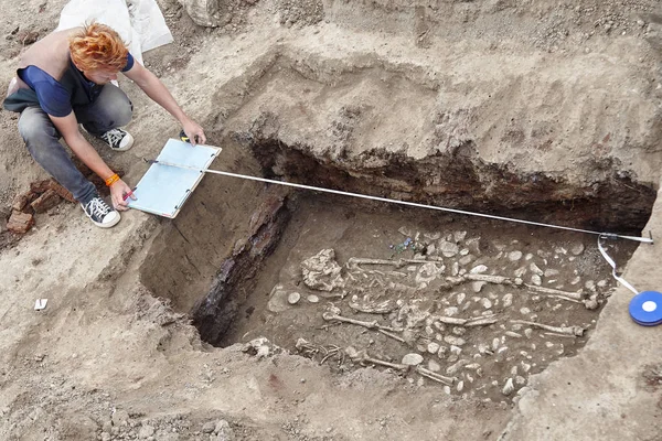 考古发掘 年轻的红头发的时尚考古学家使人类的骨骼 骨骼和头骨淹没在地下墓穴中 真正的挖掘机过程 复制空间 — 图库照片