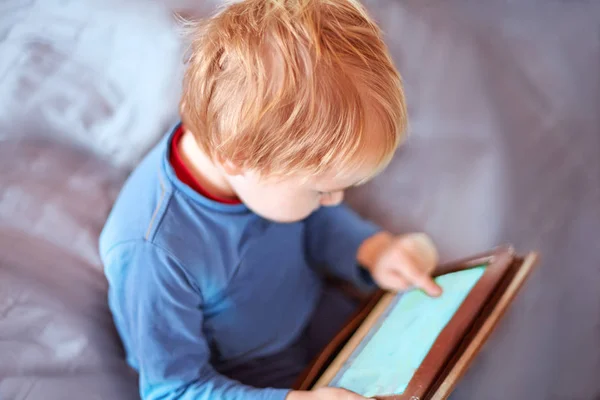 Küçük beyaz oğlu ekran dokunaklı bir tablet kullanarak kanepede oturuyor. Kızıl saçlı, rahat kıyafet, kapalı, yakın çekim, alanı Kopyala. Çocuk saat harcama, bilgisayarlaşma gençler kavramının.