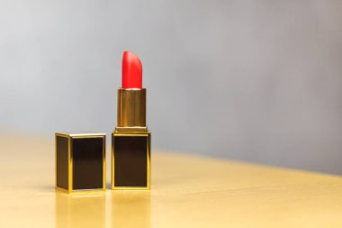 Kırmızı ruj kapağı açın, dikdörtgen şeklinde, siyah ve altın lüks Tüp, hafif ahşap masa üzerinde yerleşmiş. Şık tasarım. Gri arka plan, kopya alanı, yakın çekim.