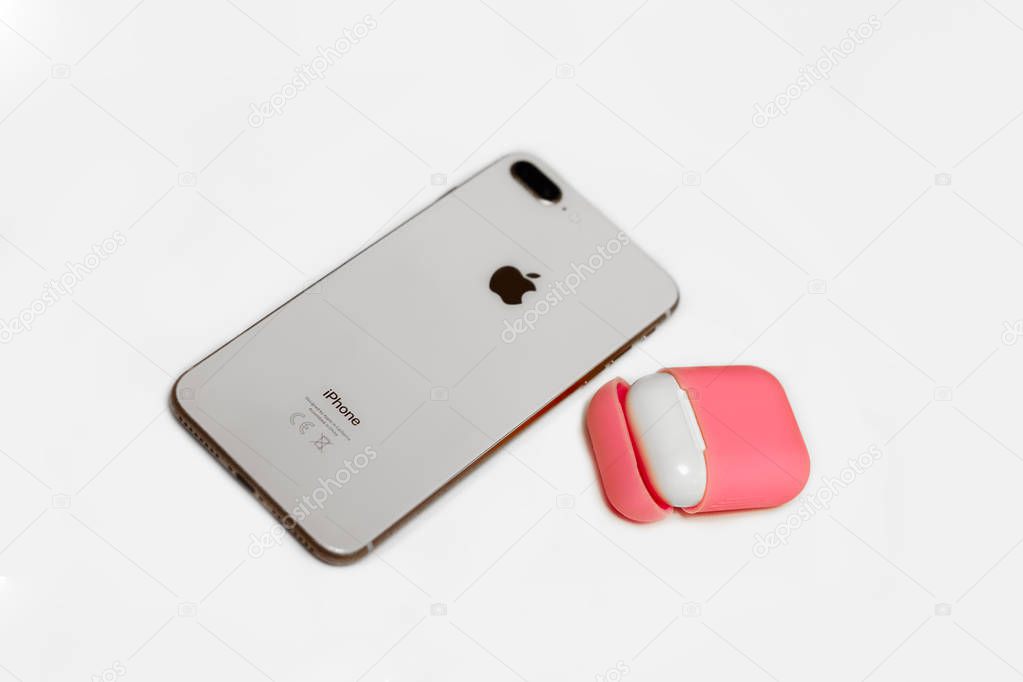 Barcelona, Spain - Jan. 2019: Little white earphones with charger box in bright pink cover box, mobile phone, chosen focus. White background, copy space, close up.