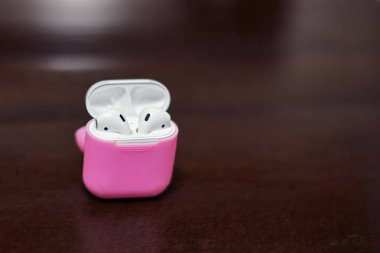Küçük beyaz kablosuz kulaklık şarj cihazı ile parlak pembe kapak kutusunda. Koyu ahşap arka plan, tarih alanı kopyalayın, yakın çekim.