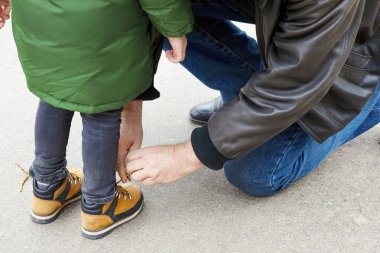 Üst düzey bir adam, bir çocuk çizmeleri üzerine bağlıyor. Baba ya da Büyükbaba onun küçük oğlu veya torunu yardımcı olur. Her ikisi de rahat giyiyor. Açık havada, kopya alanı.