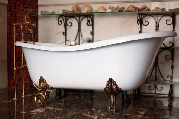Zarif iç lüks Vintage bronz ayaklı serbest ayakta Bathtube. Raflarda kabukları ile koyu sıcak renk arka plan. Seçici odaklama, iç mekanlar, kopya alanı.