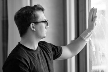 Genç yakışıklı beyaz beyaz adamın siyah beyaz portresi pencereyi süngerle yıkıyor. Koyu kıvırcık saçlı, gözlüklü, akıllı bakış, biraz hüzünlü ifade. Tek başına temizlik. İç mekanlar, kopyalama alanı.