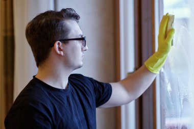 Genç yakışıklı beyaz adam pencereyi süngerle yıkıyor. Koyu kıvırcık saçlı, gözlüklü, zeki görünüşlü, hüzünlü bir ifade. Oda servisi tek başına. İçerde, boşluğu kopyala.