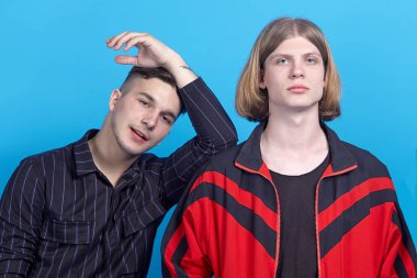 İki genç yakışıklı adam, gülümsüyor. Eşcinsel ilişki ya da yakın dostluk. Biri sarı saçlı, diğeri esmer. İç mekanlar, stüdyo portresi, kopyalama alanı, mavi arka plan.