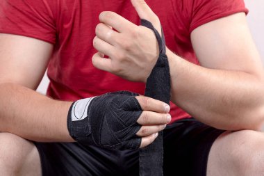 Kafkas erkek gövdesi spor kıyafetleri içinde, ellerini boks bandajlarıyla bandajlıyor, oturuyor. Maçtan ya da eğitimden önce. Kapalı alan, kopyala boşluk, kapat.