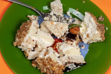 Kremalı pasta parçaları yeşil tabağa çatalla çarpmış. Diyet karşıtı konsept, sağlıksız tatlı, tatlı tutkusu, oburluk. Mercan arkaplanı, kopyala. 