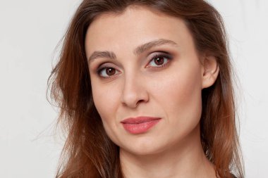 Doğu tarzında dövülmüş çekici genç bir kadının yakın portresi. Badem şeklinde kahverengi gözler, sıcak koyu saçlar, alaycı bir gülümseme, sinsi sinsi kameraya bak. Gerçek kadın, stüdyo, kopya alanı.
