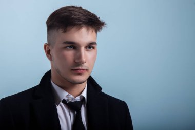 Gri mavi arka planda özenli görünümlü yakışıklı bir adamın portresi. Moda saç stili, etkileyici yüz, küçük sakal, klasik resmi siyah takım elbise. Stüdyo, kopyalama alanı.