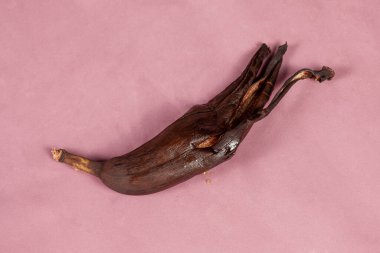 Bozuk bir muz, yarı soyulmuş ve çürümüş, mor bir arka planda yatıyor. Bayat meyve konsepti. İçerde, boşluğu kopyala.