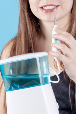 Diş sağlığı ekipmanlarını kapatın, ağız temizleyicisi, genç bir bayana sarılın, gülümseyin ve beyaz dişlerinizi gösterin. Kapalı alan, mavi arkaplan, kopyalama alanı. 